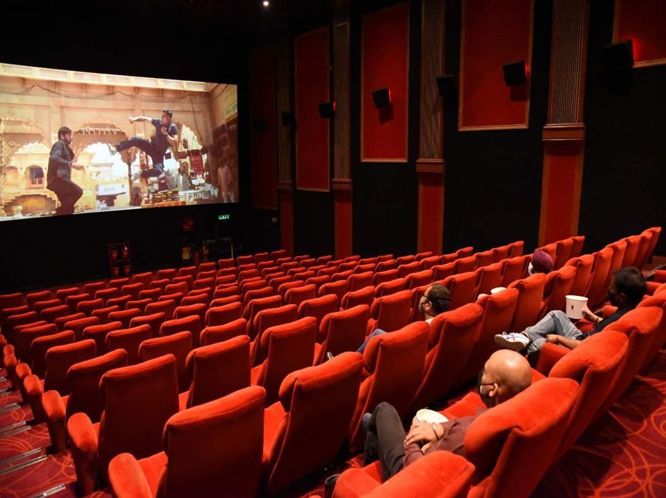 Audience in cinema theater watching cultural action film with traditional costumes and historical architecture.