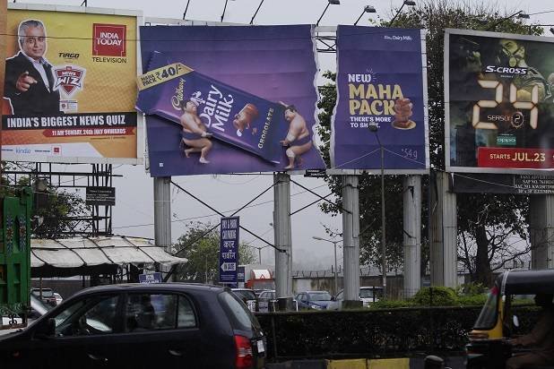 Roadside billboard hoarding advertising displaying multiple brand campaigns along a busy city street for outdoor advertising visibility.