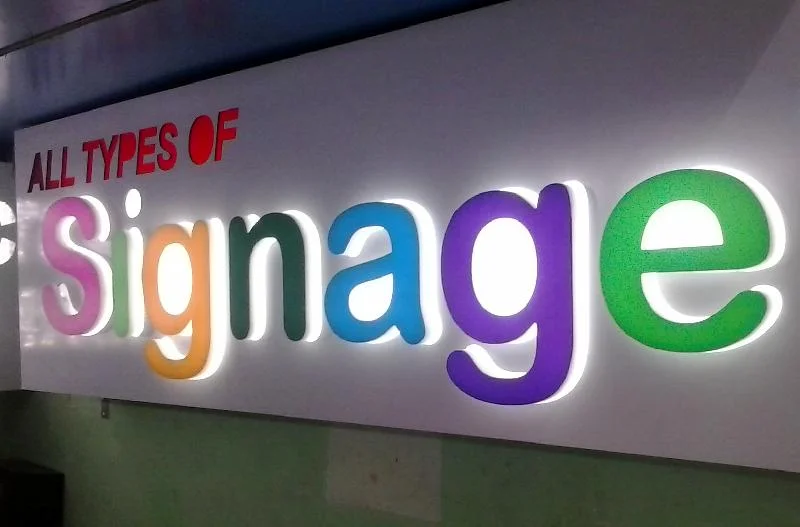 "Colorful 3D backlit signage board with text 'All Types of Signage' on a wall"