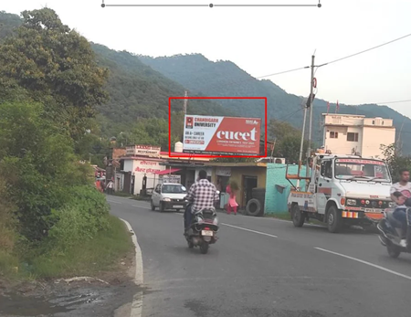 Hilly road scene in Himachal Pradesh with 20x10 ft Chandigarh University hoarding by ACME Advertising Co., promoting CUCET scholarship test; visible motorcycles, truck, roadside buildings, and curved highway.