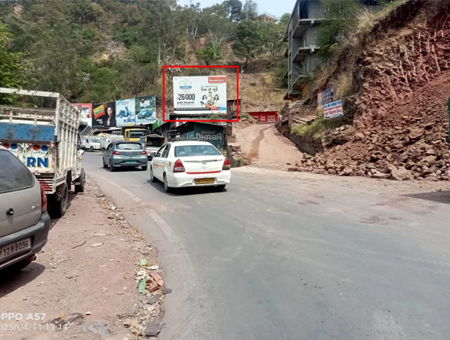 Hilly highway scene in Himachal Pradesh with 20x10 ft BYJU'S hoarding by ACME Advertising Co., promoting smart classes for students; visible trucks, cars, roadside slope, and hillside buildings